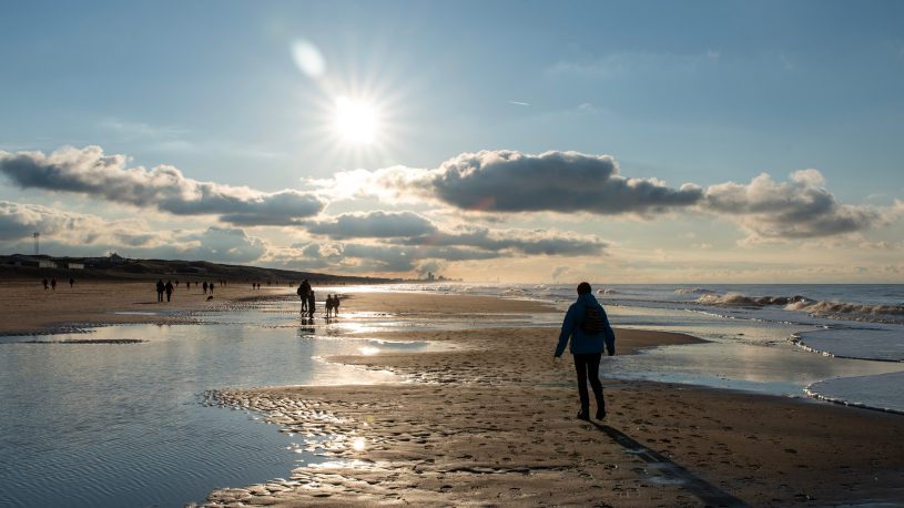People walking along a peaceful beach at sunset with stunning cloud formations and reflections.