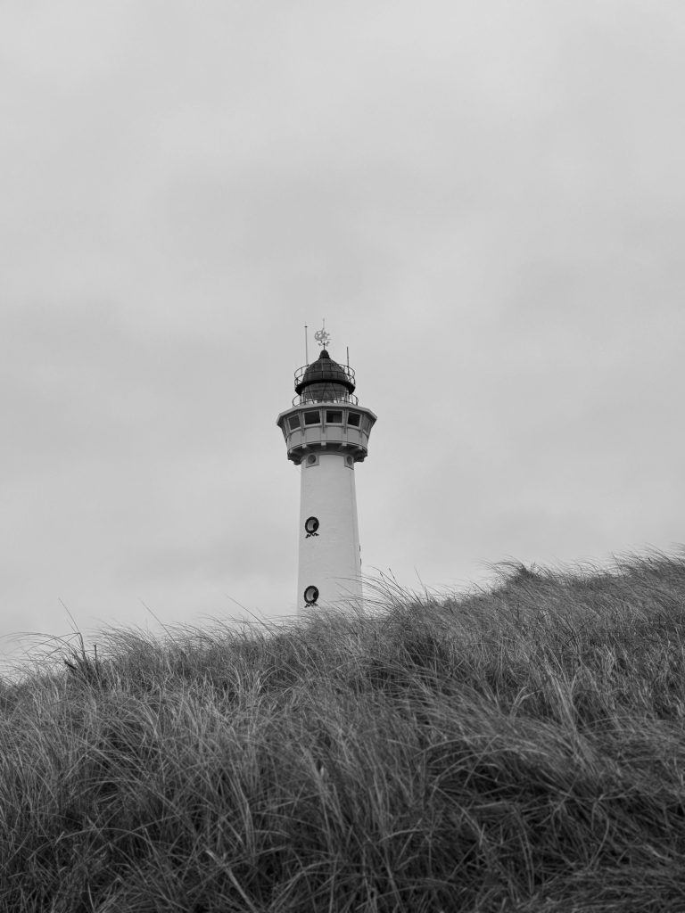 Black and white photo of Egmond aan Zee lighthouse behind sand dune grass.